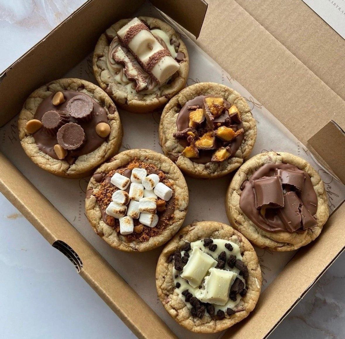 Assorted cookie pies with chocolate and marshmallow toppings in a box.